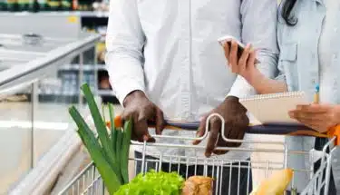couple with shopping cart checking on mobile shopping list at supermarket